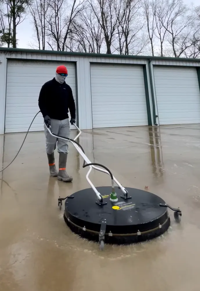 Crew member running a large surface cleaner across concrete